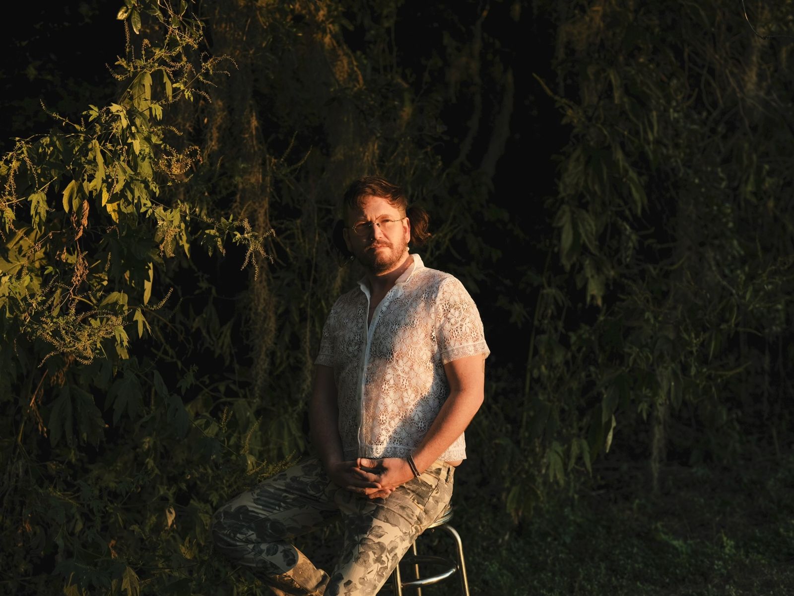 Cory Diane seated on a stool in golden evening light, in front of dense green foliage and Spanish moss.